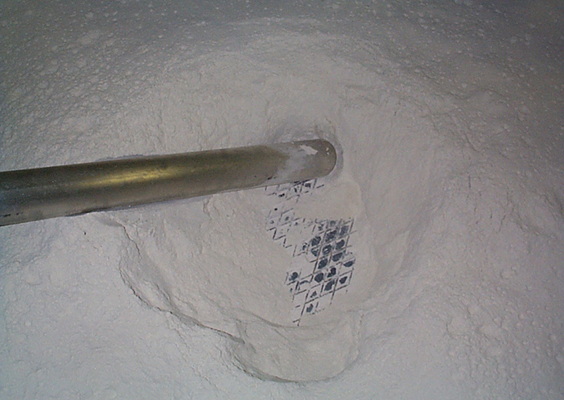 Industrial suction hose submerged in a fine white powder, demonstrating the BEAD filter separator's capability to handle high-volume or dusty materials like ash, cement, or lime.
