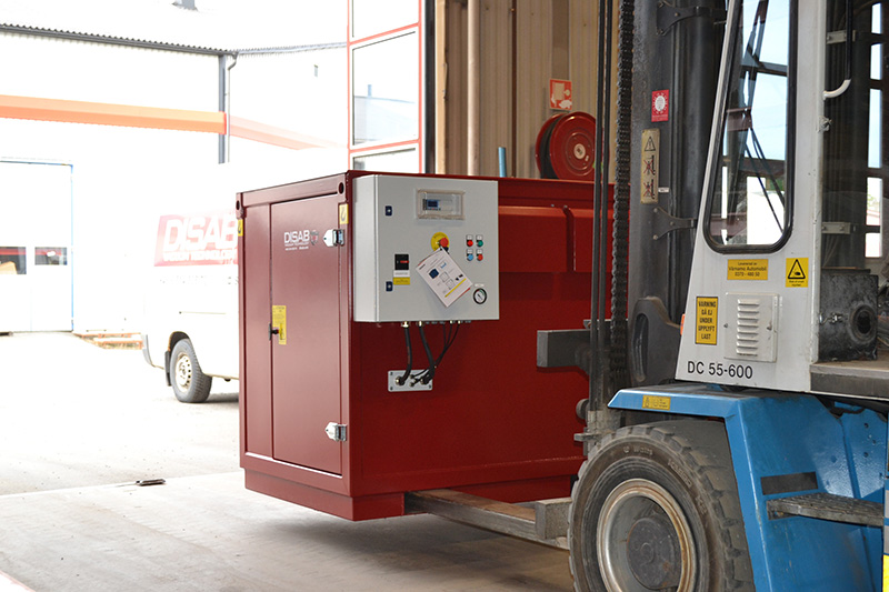 Red DISAB standalone vacuum unit being transported by forklift in an industrial setting, showcasing its integrated lifting loops, compact design, and control cabinet for safe and mobile operation.