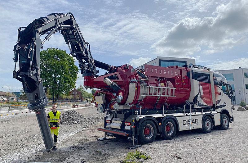 Red DISAB Futurion™ Q20 MultiFLEX vacuum loader parked on a construction site with its articulated hose arm raised, demonstrating long-range suction and digging capabilities for industrial applications.