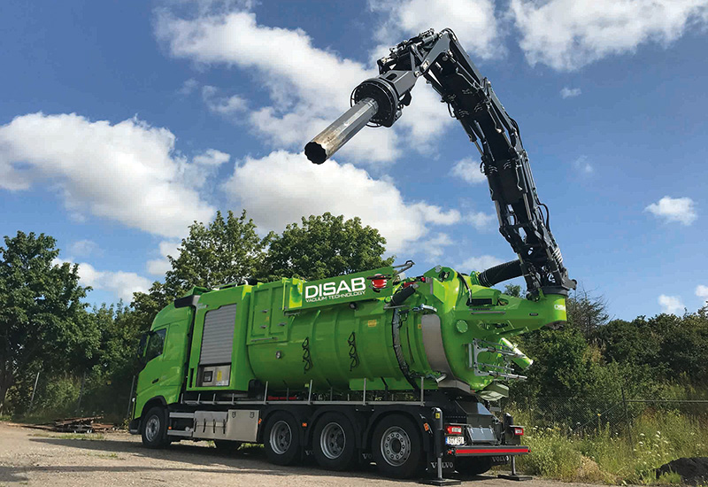 Green DISAB Futurion™ Q10 MultiFLEX vacuum loader parked outdoors with its long-range hose arm extended high into the air, illustrating its ability to handle both wet and dry materials in complex environments.